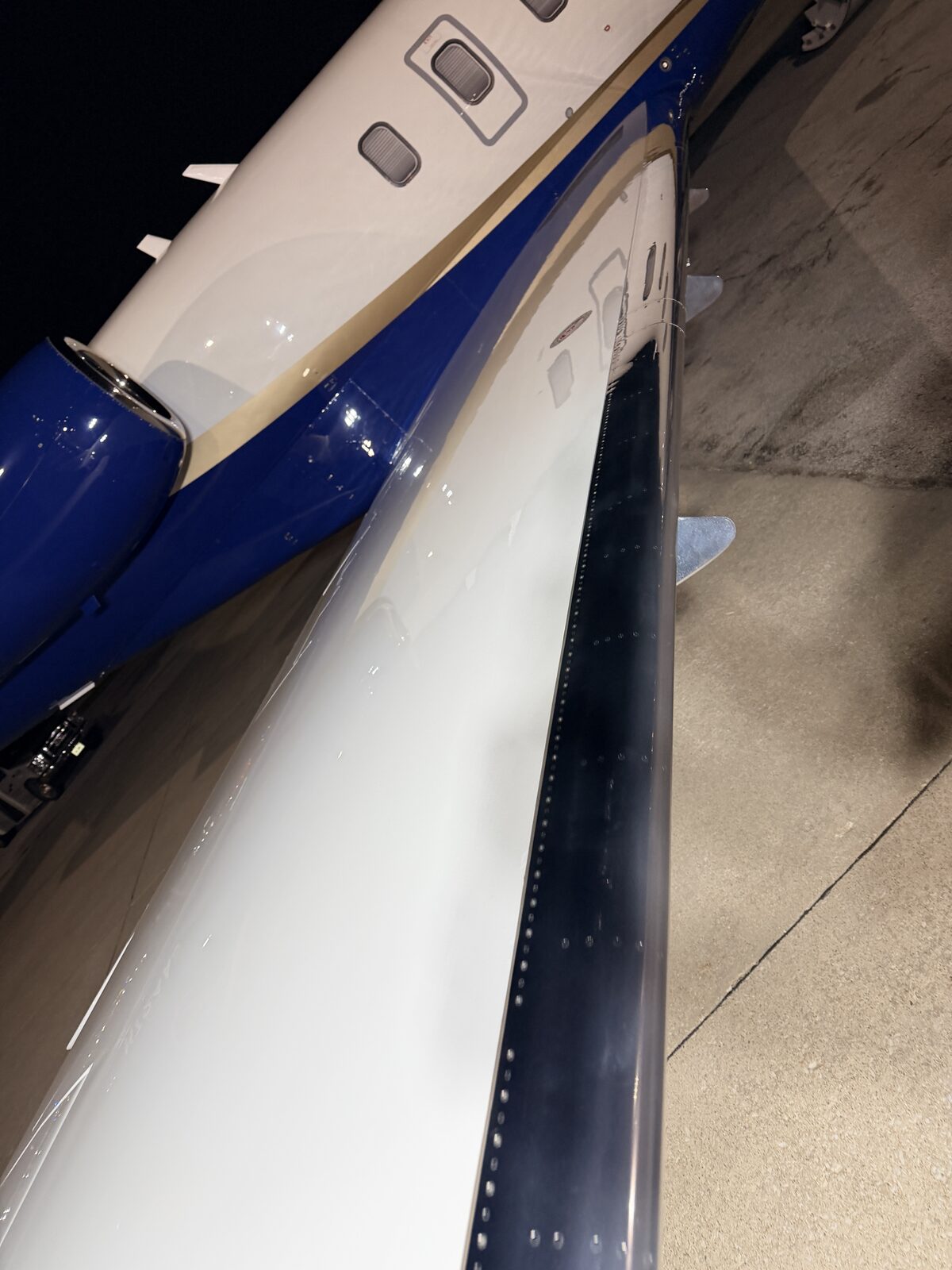 After: Challenger 350 wing and fuselage exterior showing blue and white livery with engine nacelle at night