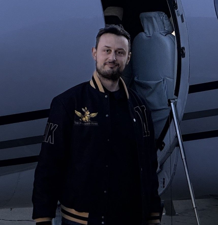 Michael Koutsostamatis, founder of The Polished Hare, standing beside a private jet on the ramp wearing a Polished Hare branded jacket