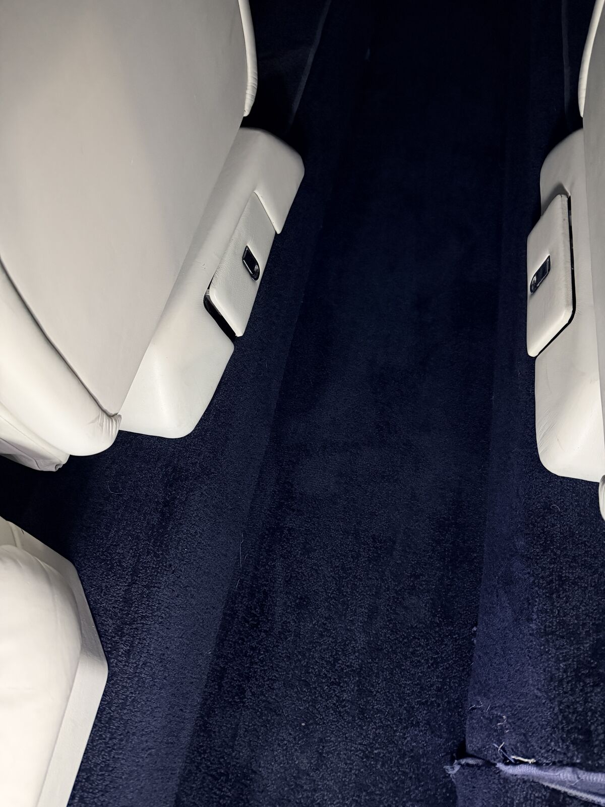 Private jet white leather passenger seats with navy blue sidewall carpet between them after interior detailing