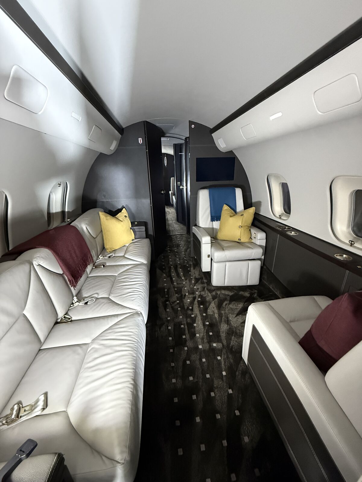Luxury private jet cabin with white leather seating, yellow accent pillows, burgundy throw, and patterned carpet after interior detailing