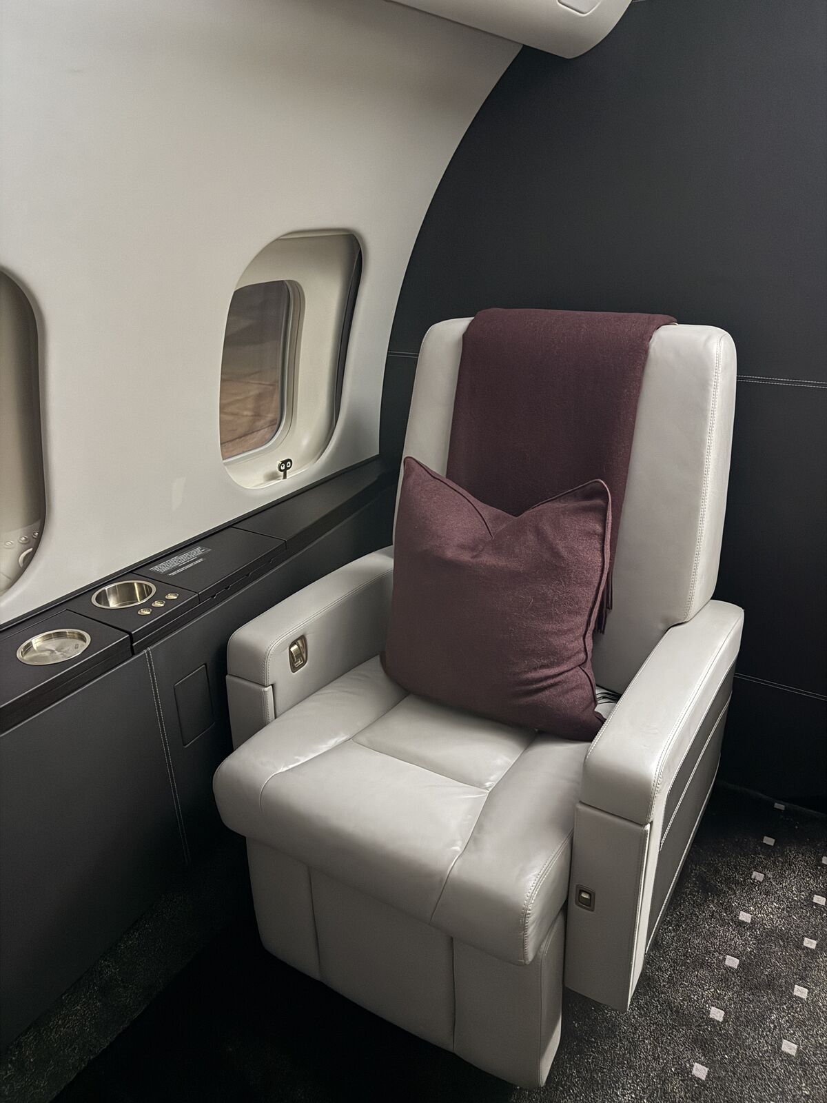 Private jet white leather passenger seat with burgundy accent pillow, cabin window, and sidewall ledge after interior detailing
