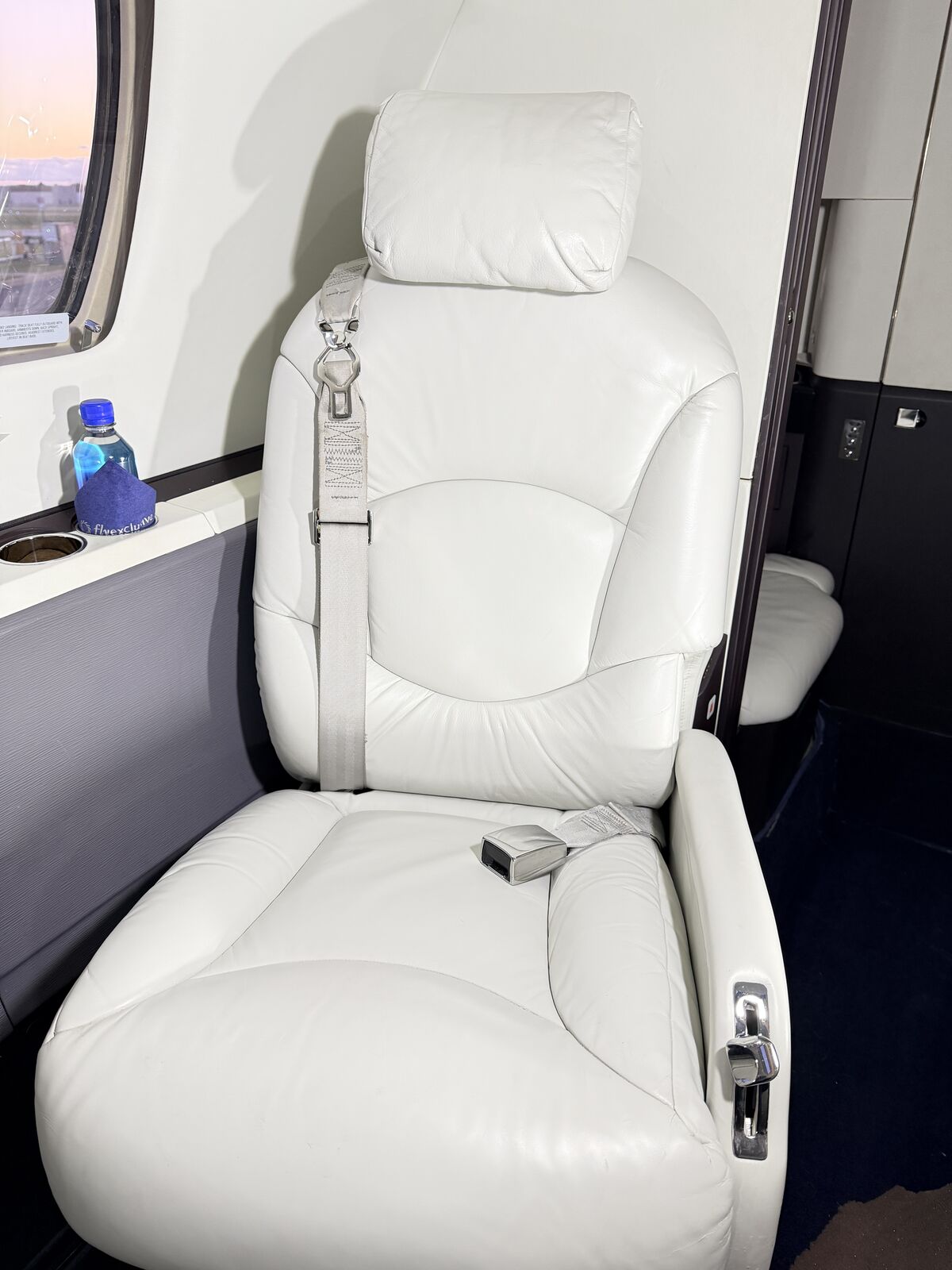 Private jet white leather passenger seat pair with seatbelt hardware and gray floor panel after interior detailing