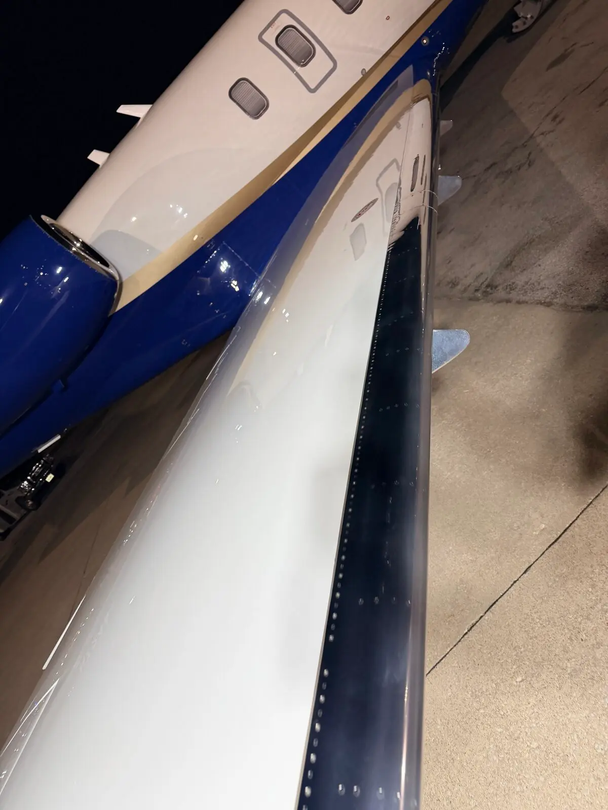 After: Challenger 350 wing and fuselage exterior showing blue and white livery with engine nacelle at night