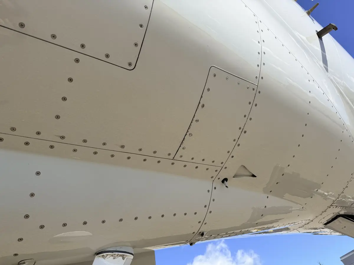 Close-up of cleaned Cessna Citation X fuselage paint, rivet lines, and access panel showing an even, contaminant-free finish against blue sky
