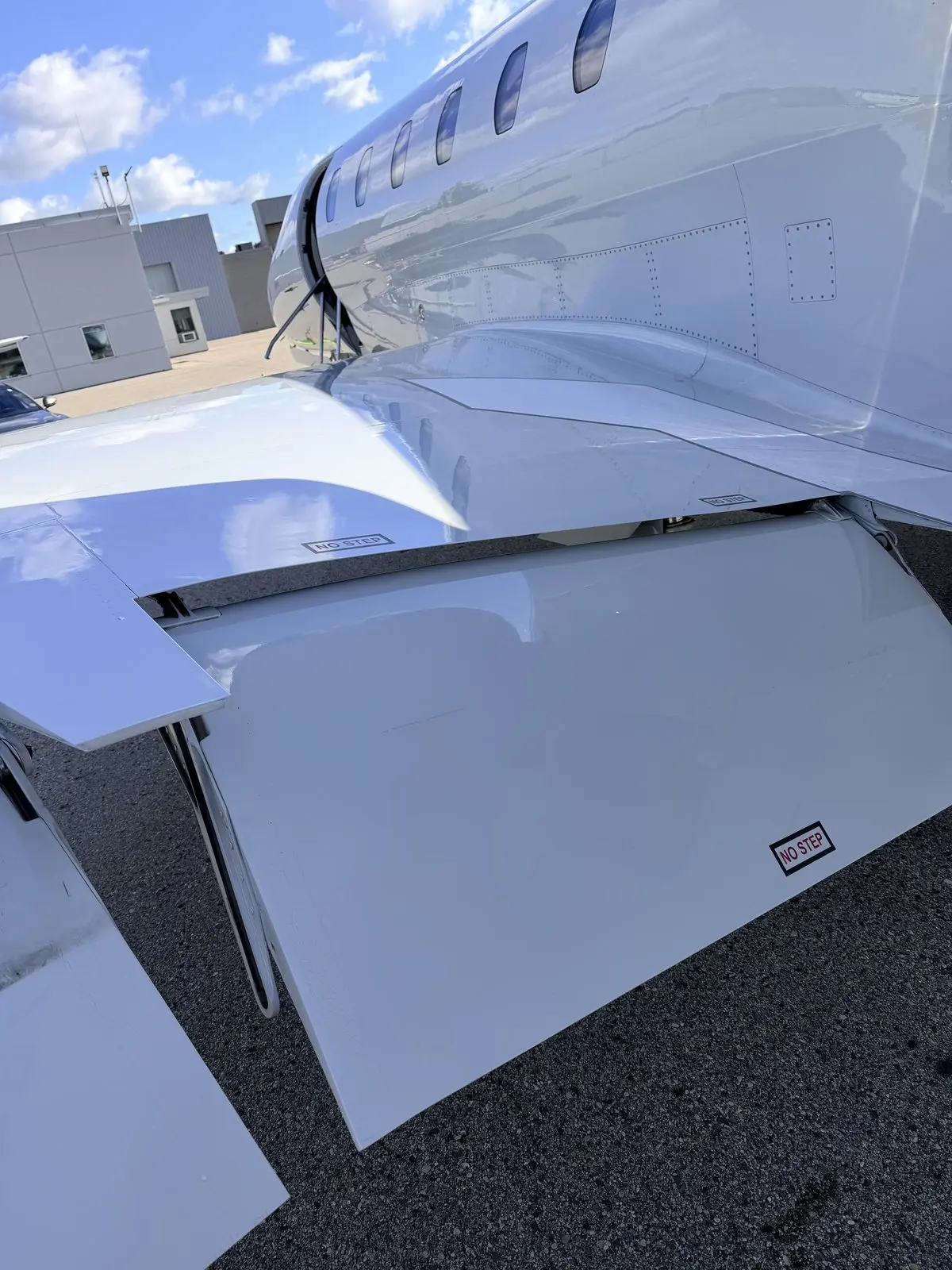 Cleaned wing root, flap fairing, and NO STEP markings on a Cessna Citation X with a glossy white topcoat reflecting the FBO ramp