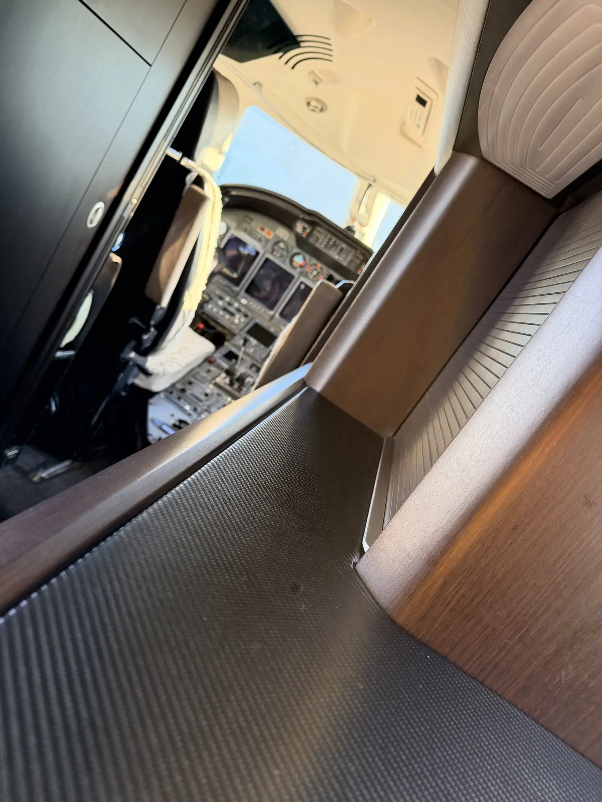 Carbon-fiber and wood veneer cabinetry surfaces in the forward cabin of a Cessna Citation X, with the flight deck visible through the open cockpit doorway