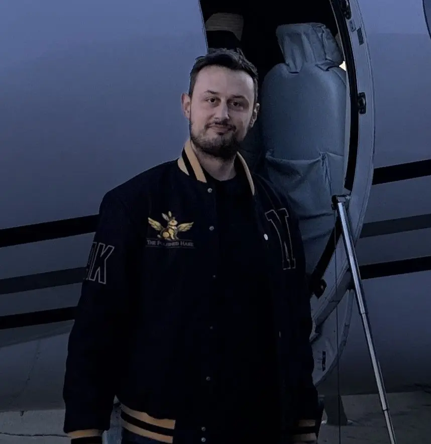 Michael Koutsostamatis, founder of The Polished Hare, standing beside a private jet on the ramp wearing a Polished Hare branded jacket