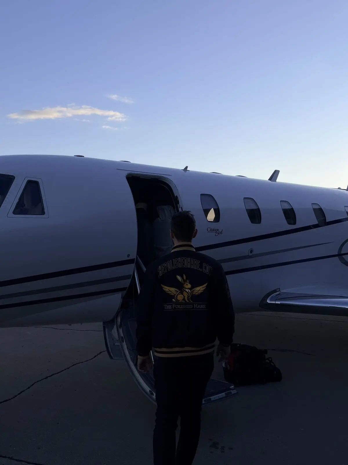 The Polished Hare aviation detailer boarding Cessna Citation Excel wearing branded jacket with equipment bag on ramp at dusk