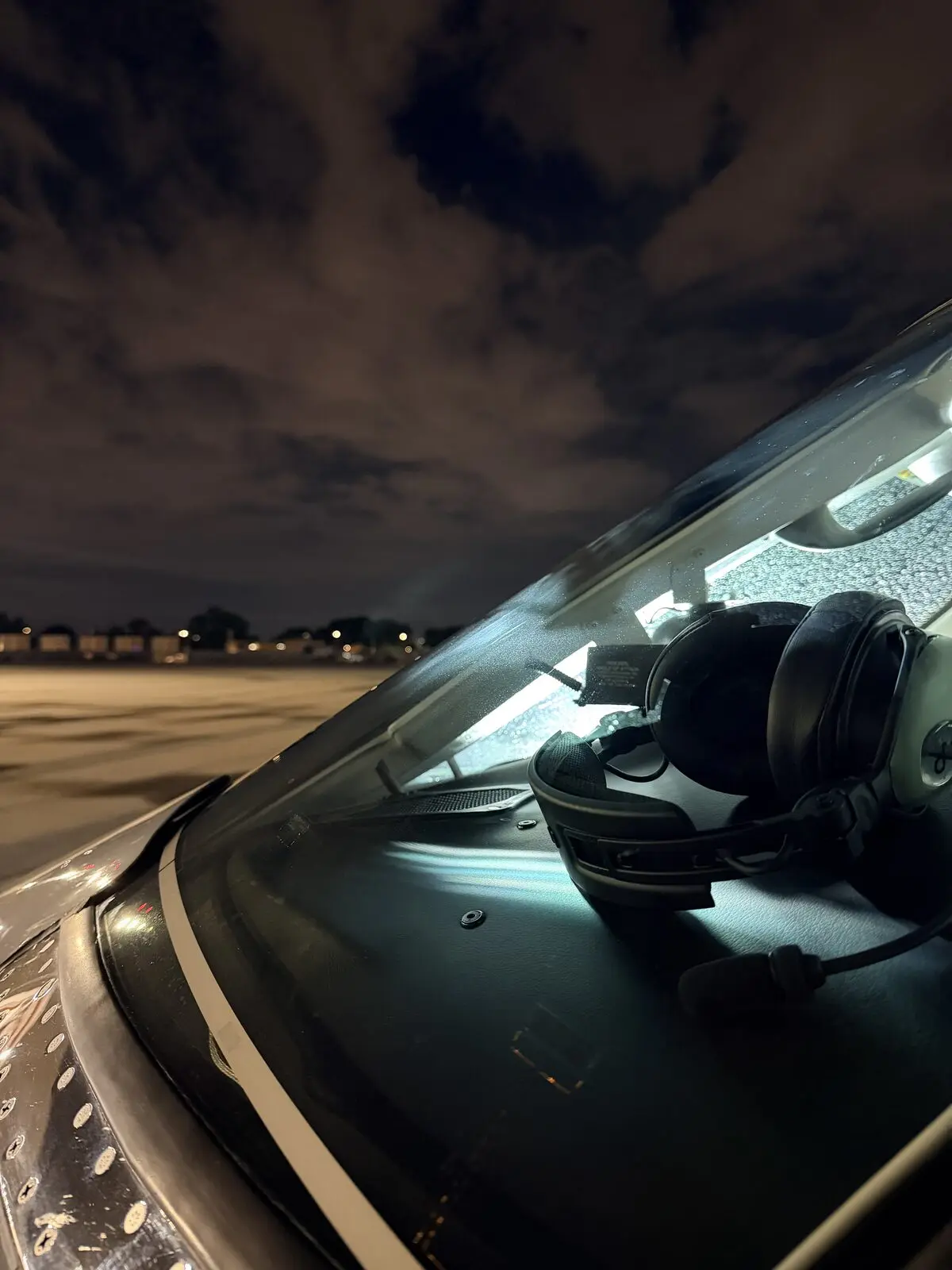 Cessna Citation X cockpit windshield and headset visible through glass with night sky and ramp lights after exterior detail
