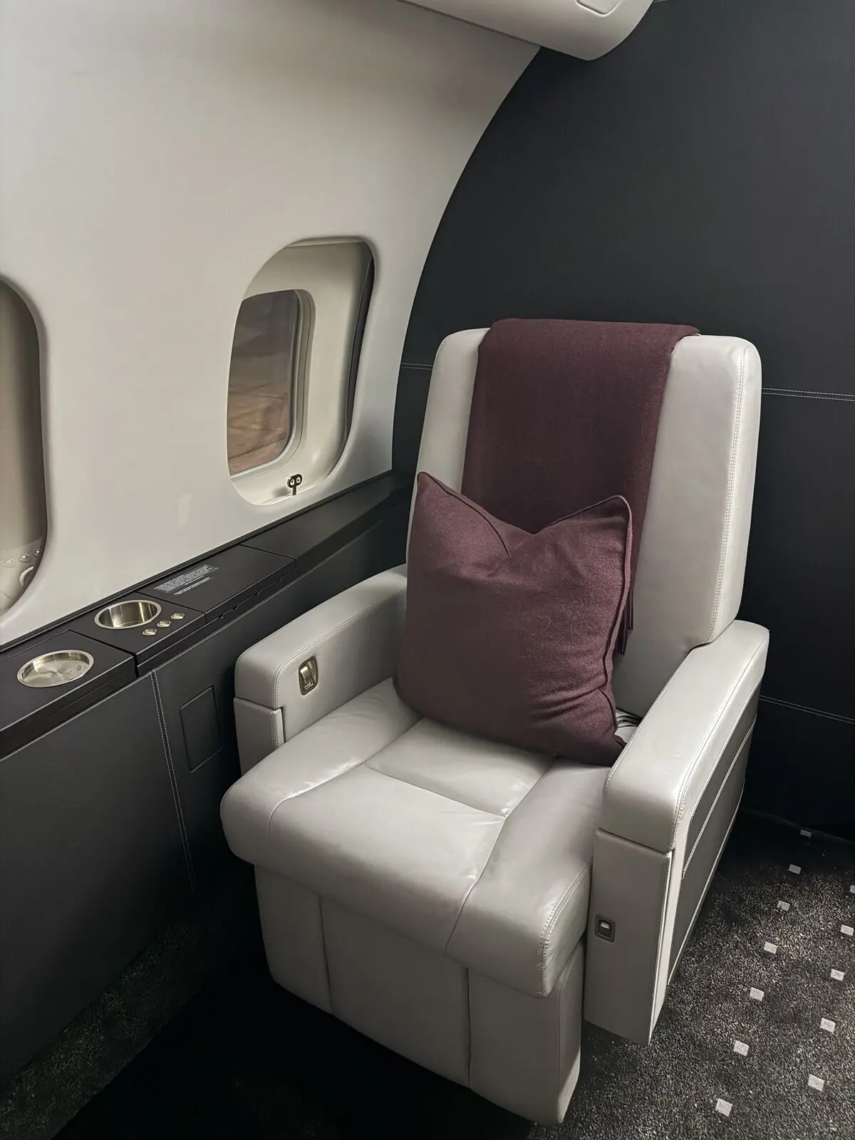 Private jet white leather passenger seat with burgundy accent pillow, cabin window, and sidewall ledge after interior detailing