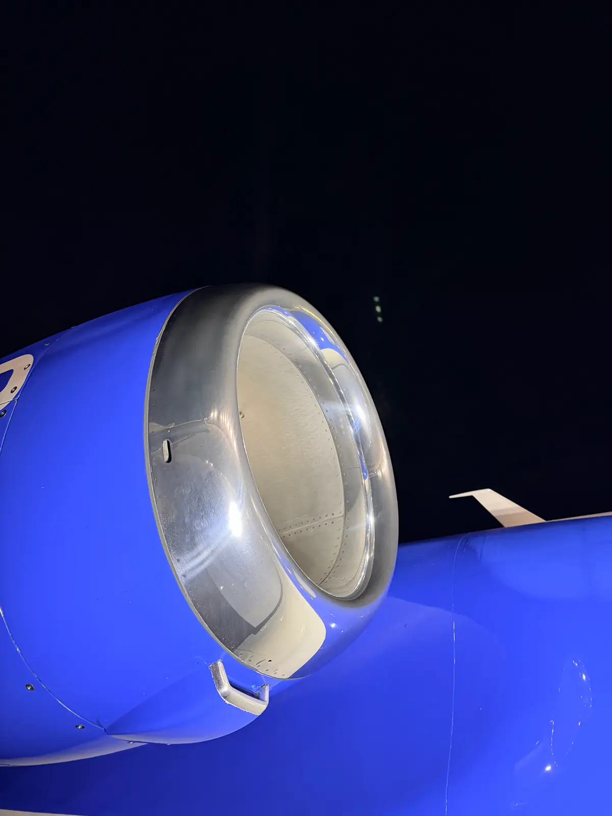 Embraer Phenom 300 fuselage side with cabin windows, blue cheatline, and glossy white belly at night after exterior detailing