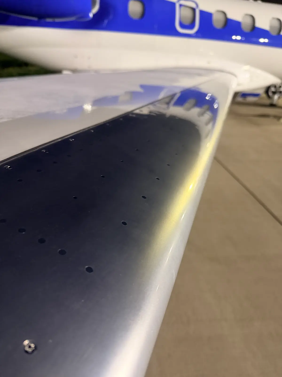 Embraer Phenom 300 polished metal wing leading edge with blue and white fuselage and cabin windows behind at night