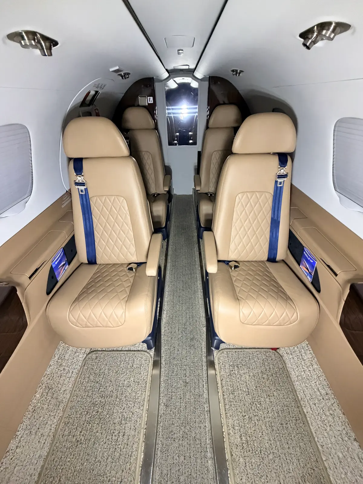 Embraer Phenom 300 cabin looking forward with tan diamond-quilted club seats, clean aisle carpet, and polished wood cabinetry after interior detailing