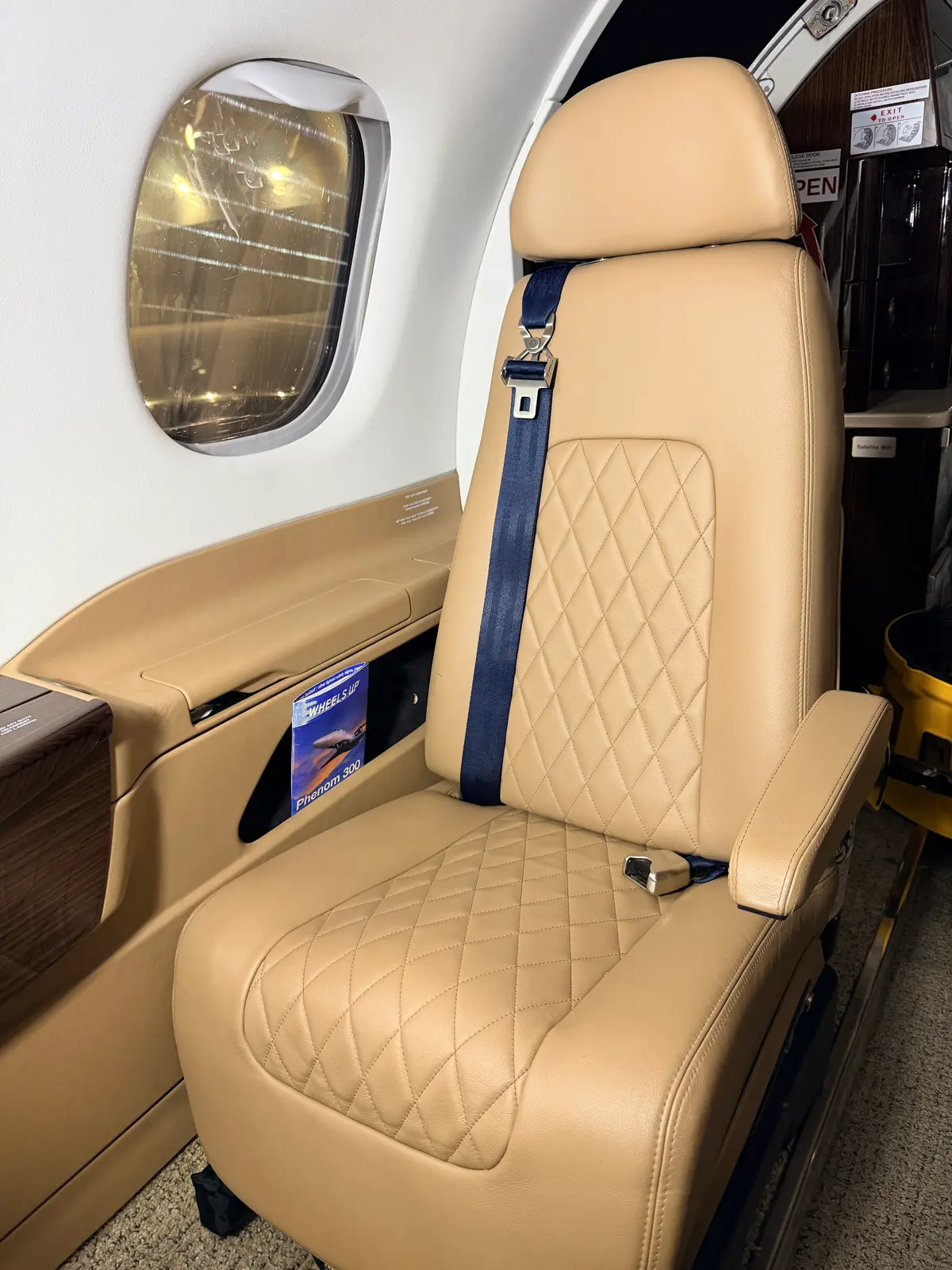 Embraer Phenom 300 tan diamond-quilted leather passenger seat with navy blue seatbelt and cabin window after interior detailing